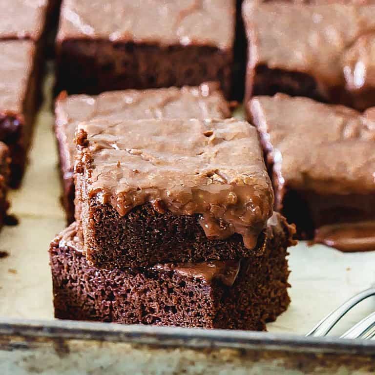 Dripping iced chocolate cake squares on metal pan.