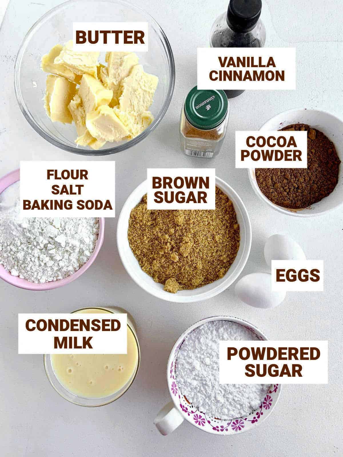 Bowls with chocolate cake ingredients on light colored surface including condensed milk, flavorings. Brown text overlay.