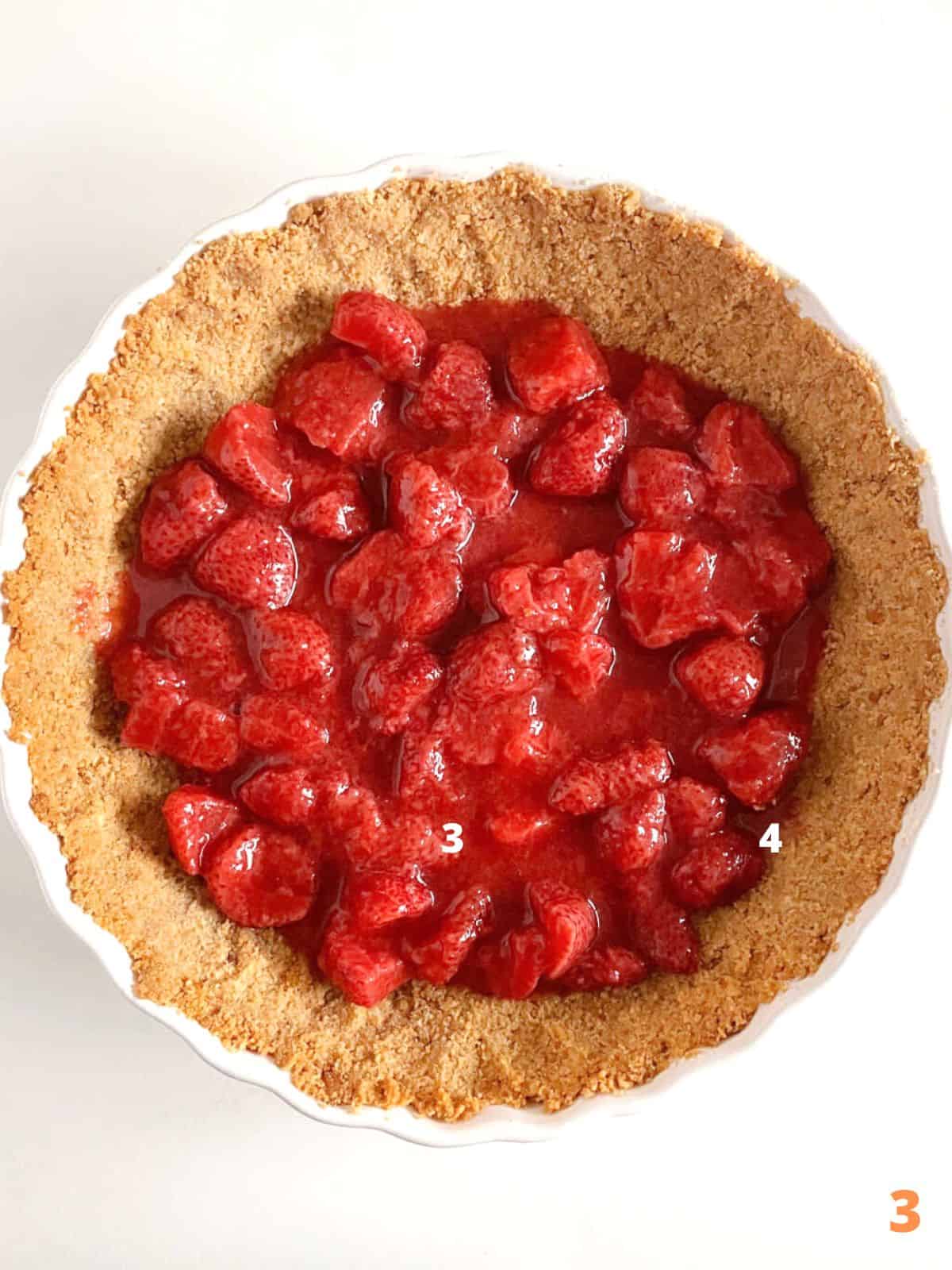 Top view of strawberry pie filling in a graham cracker crust, white surface.