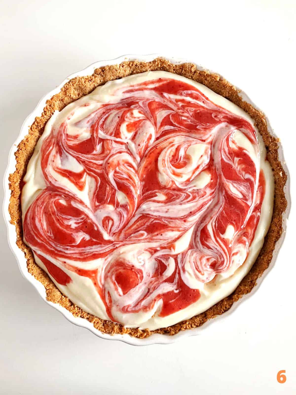 Swirled strawberry cream cheese pie with crumb crust in white dish on a white surface.