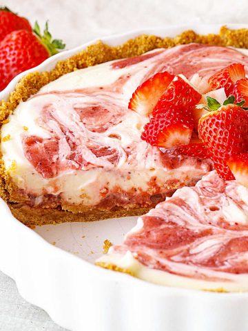 Round white pie dish with frozen strawberry swirl pie, a slice missing, fresh strawberries on top.