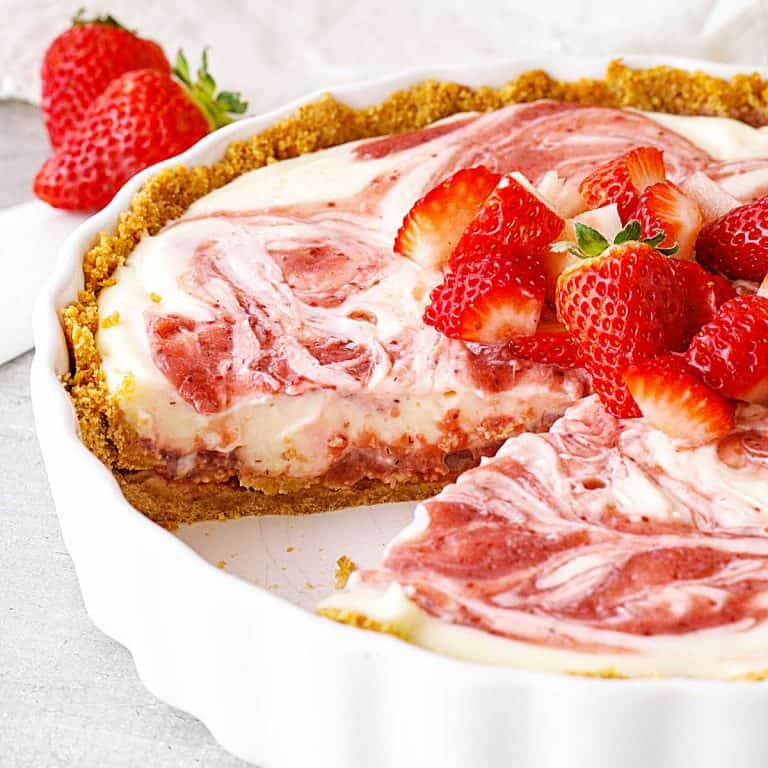 Round white pie dish with frozen strawberry swirl pie, a slice missing, fresh strawberries on top.