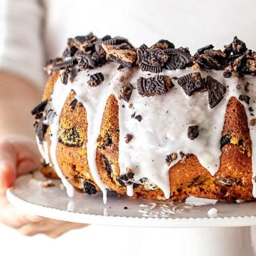 Partial view of glazed Oreo topped vanilla pound cake on a white cake stand.