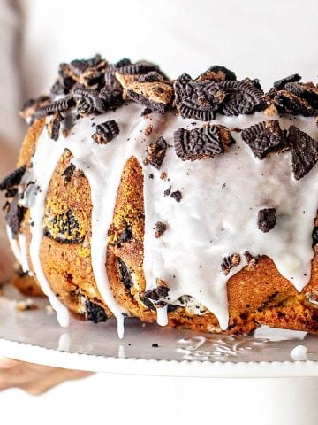Partial view of glazed Oreo topped vanilla pound cake on a white cake stand.
