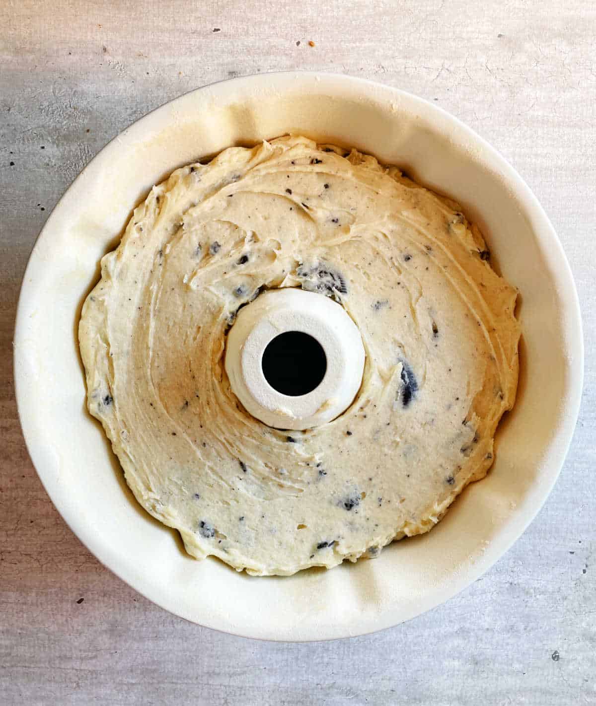 Top view of unbaked vanilla oreo cake batter in white bundt pan on a grey surface. 
