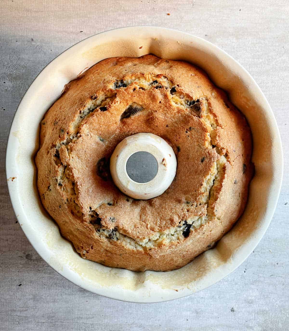 Baked vanilla oreo bundt cake in white pan on a grey surface.