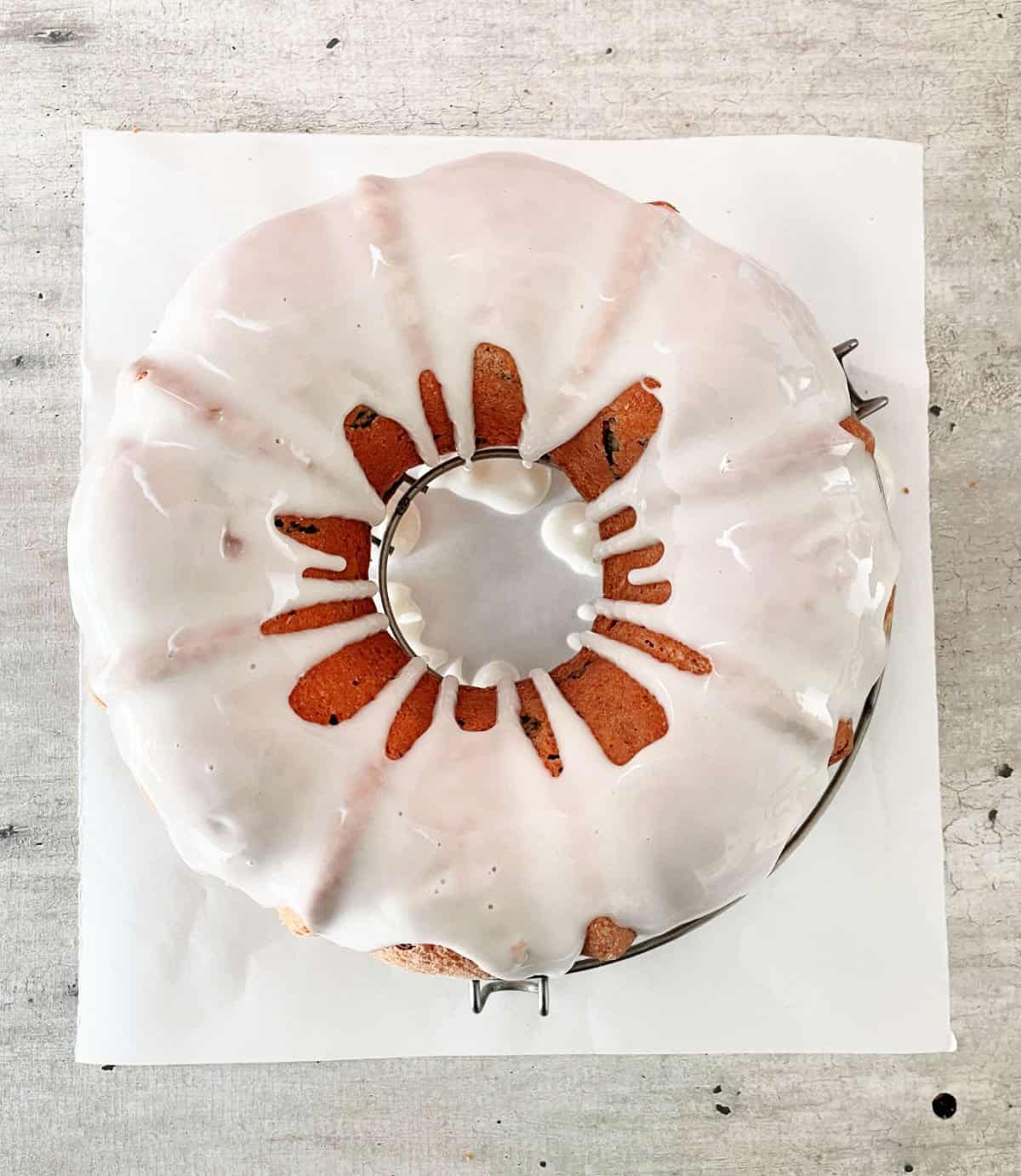 Glazed bundt cake seen from the top on a white paper set on a grey surface.