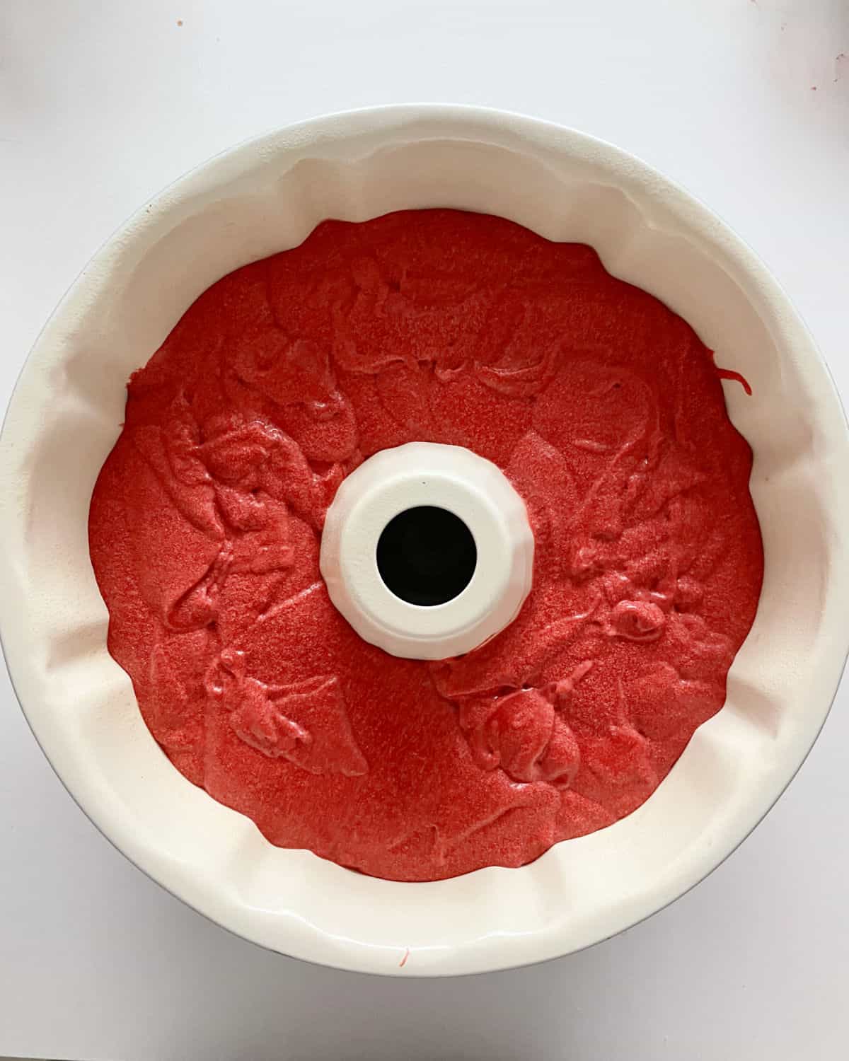 Red velvet cake batter in white bundt pan on white surface; top view.