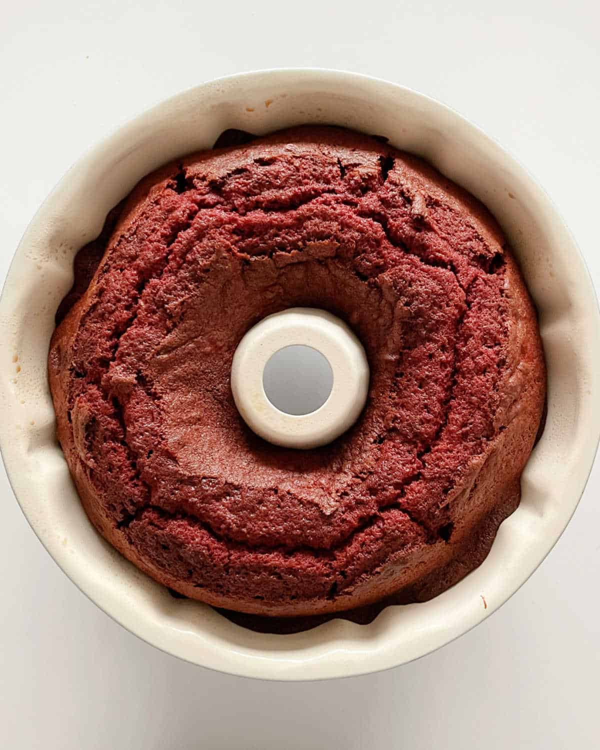Top view of baked red velvet bundt cake in white pan on a white surface.