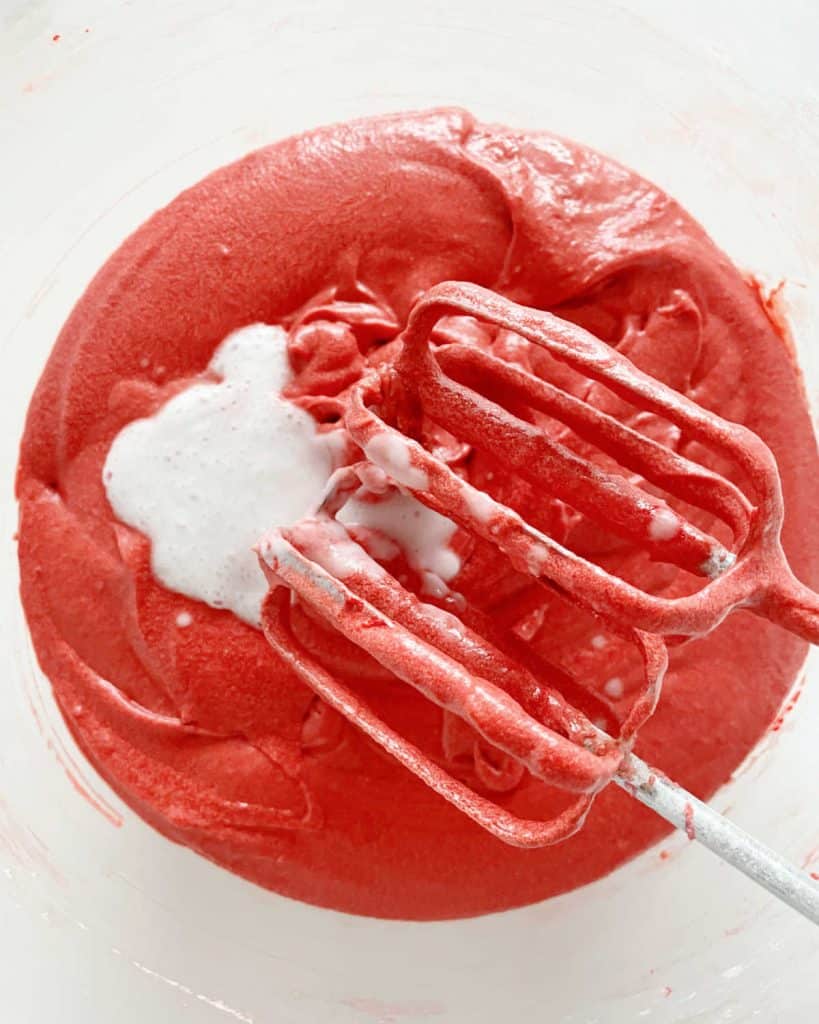 Adding baking soda to red velvet cake batter in glass bowl.