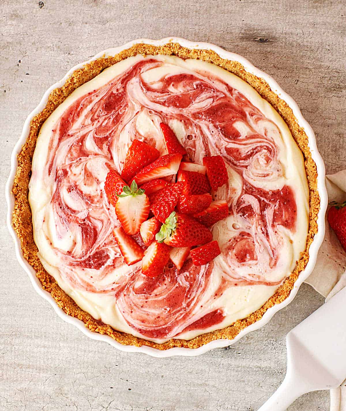 Top view of whole straberry swirl pie on a white dish on a grey surface.