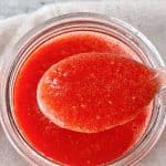 White and red text overlay over image of spoon and jar with strawberry puree, grey background.
