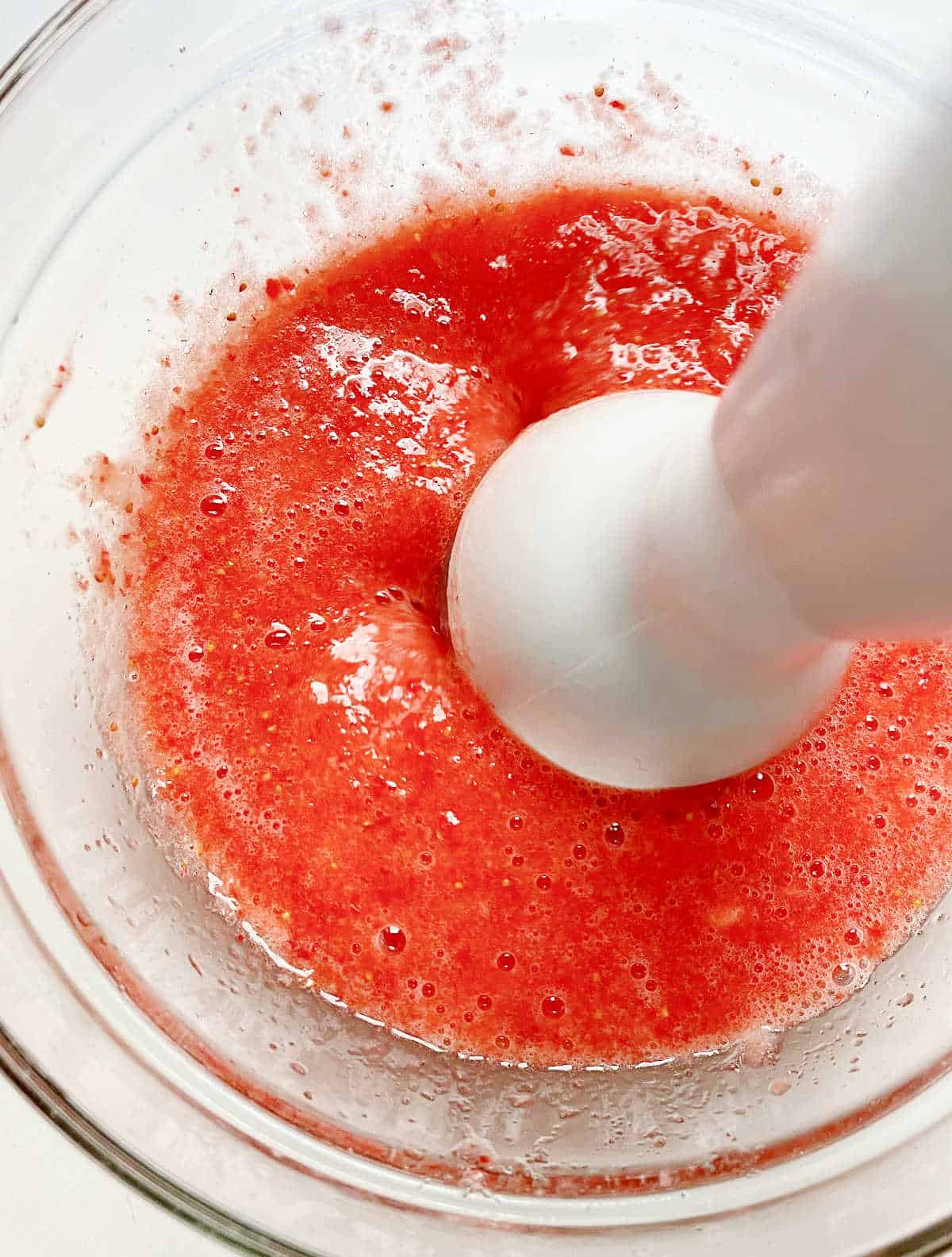 Strawberry puree in glass bowl with immersion blender.
