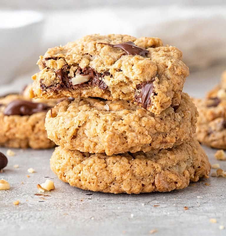 Close up of eaten oatmeal chip cookie on top of stack of cookies on grey surface.