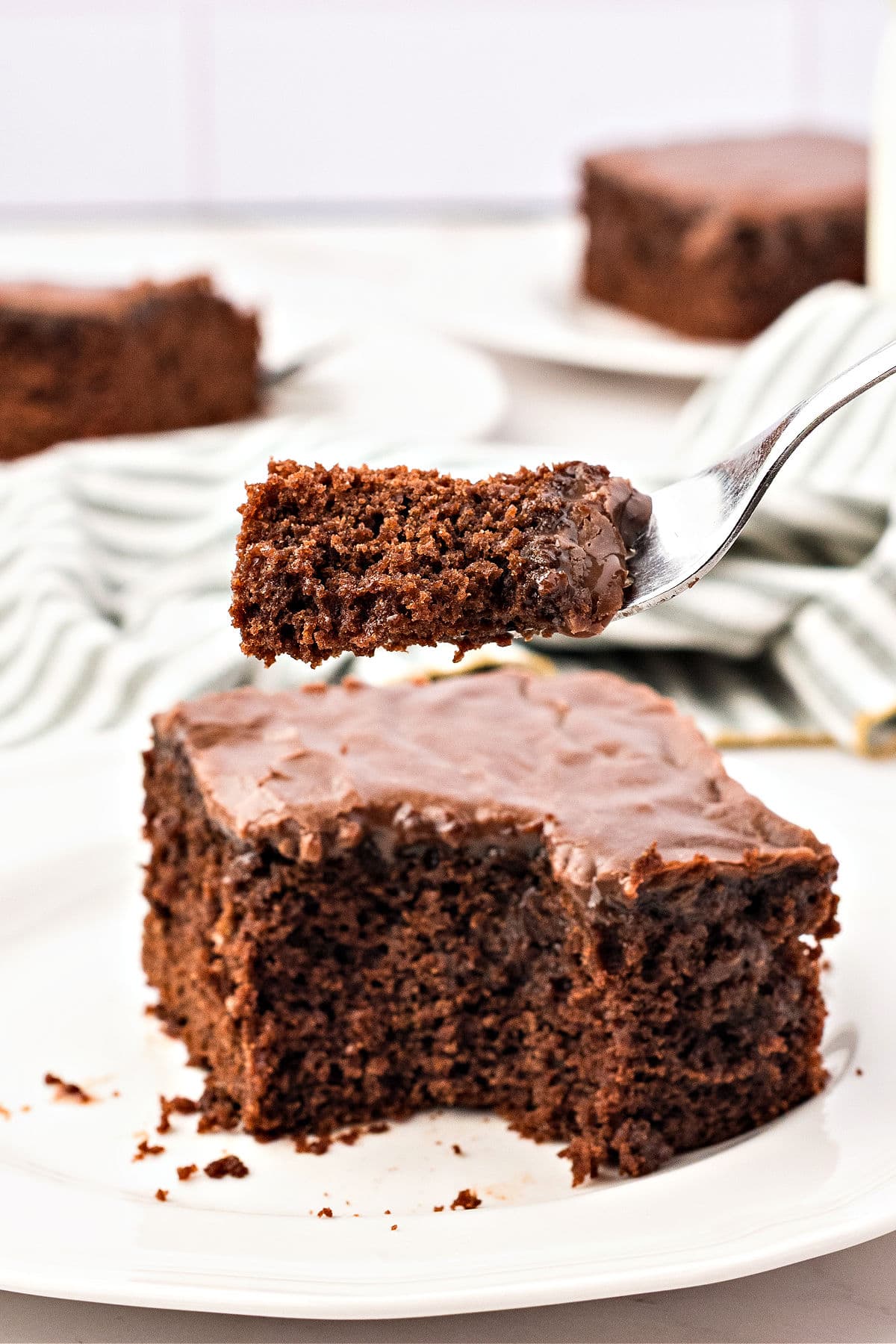 Forked bite of iced condensed milk chocolate sheet cake on a white plate.