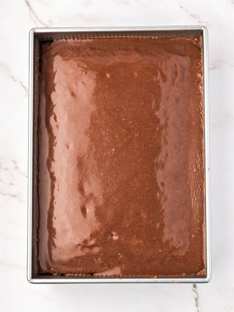 Wet icing on rectangular chocolate cake in a metal pan. Marbled background.