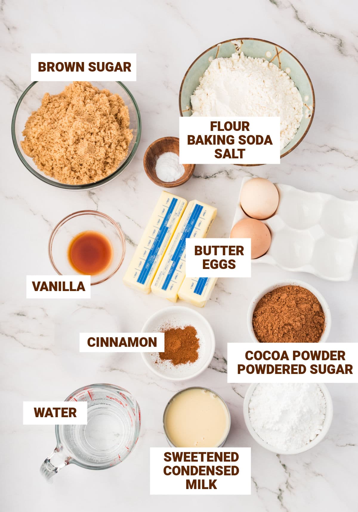 Ingredients for chocolate condensed milk cake in bowls on white marble.