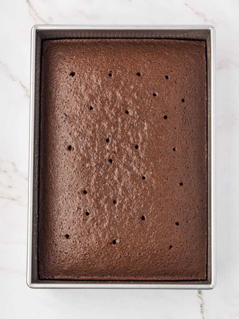 Baked and poked chocolate rectangular cake in metal pan. Marbled background.