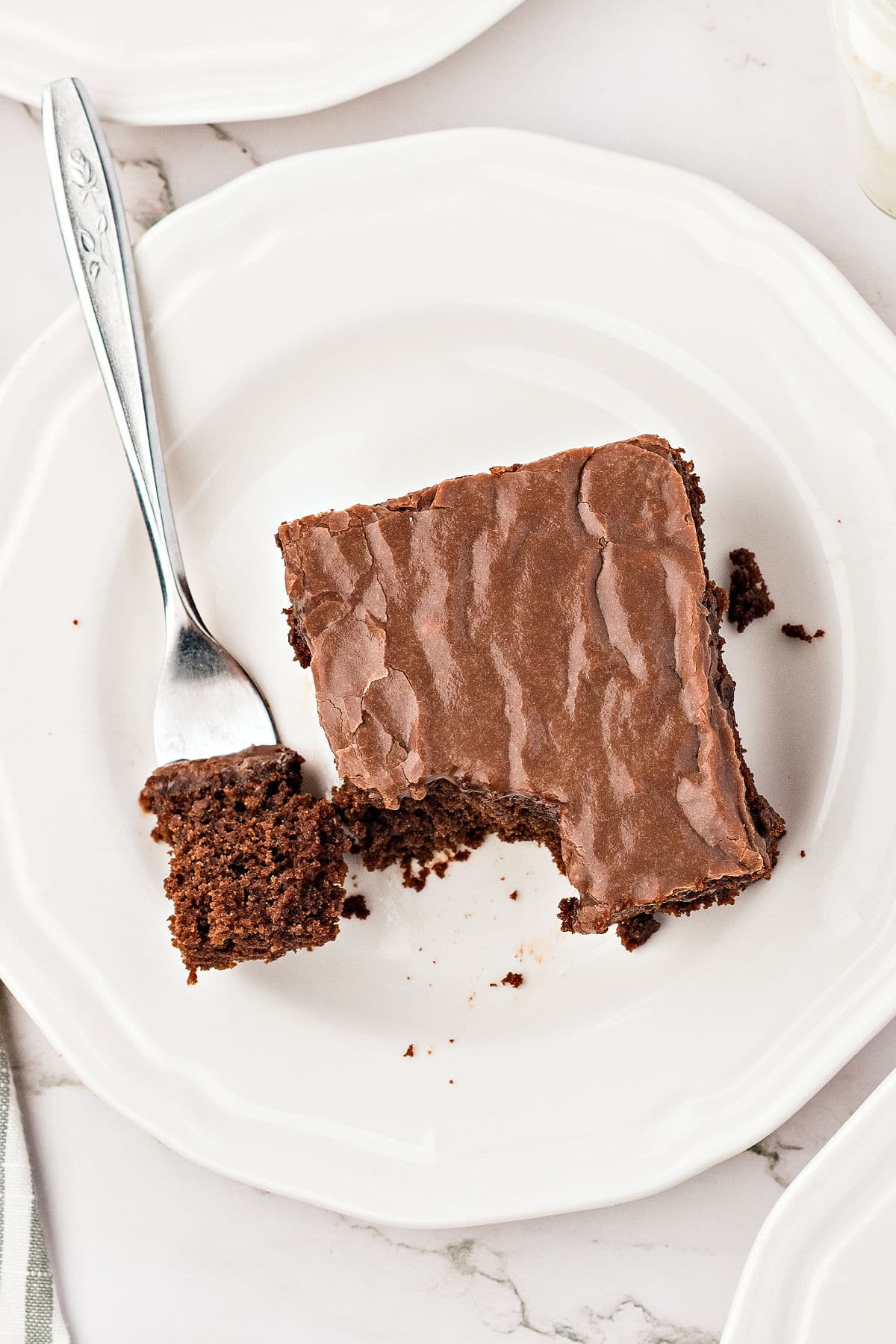 Serving of iced chocolate cake on a white plate. Silver fork. White background.