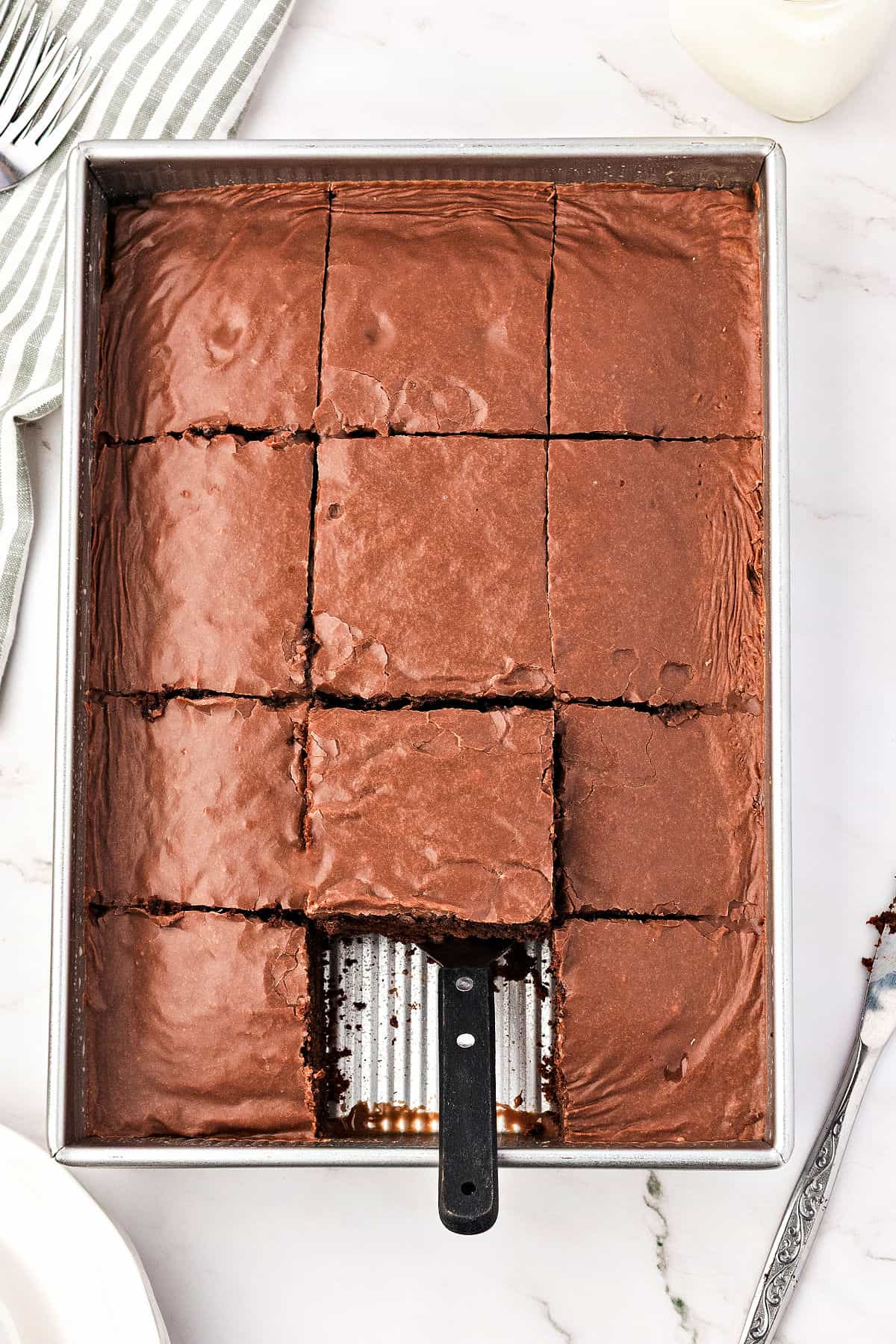 Frosted chocolate rectangular cake in metal pan. Square missing. Marbled background. 