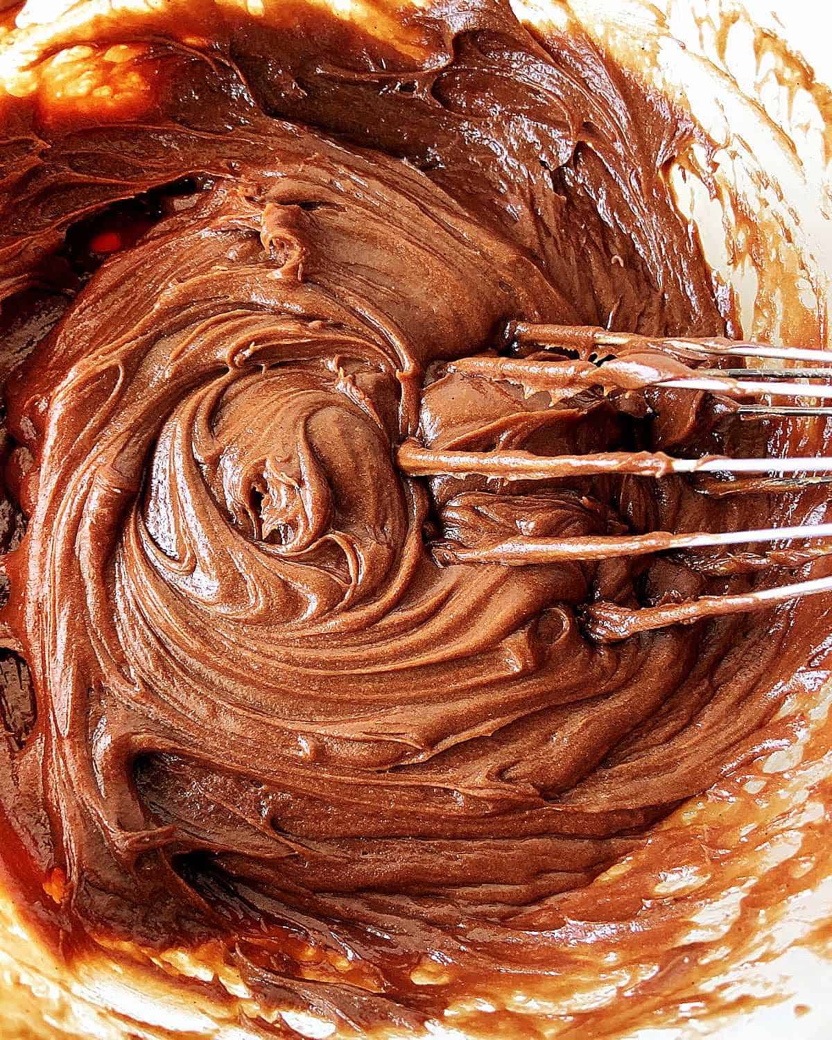 Glass bowl with whipped chocolate frosting. Wire whisk inside.