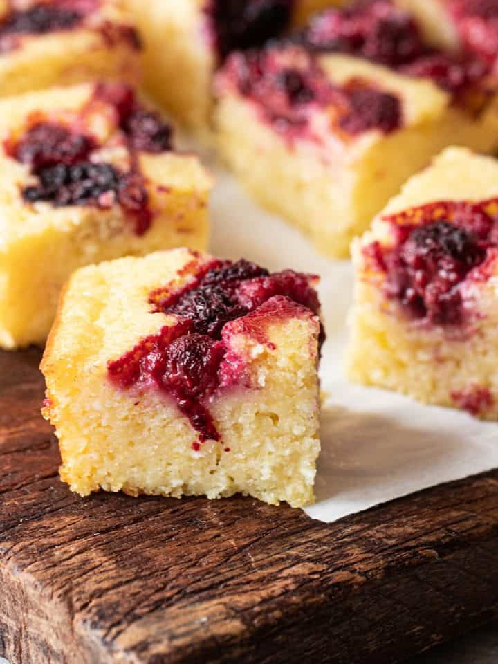 Dark wooden board with berry ricotta cake squares.