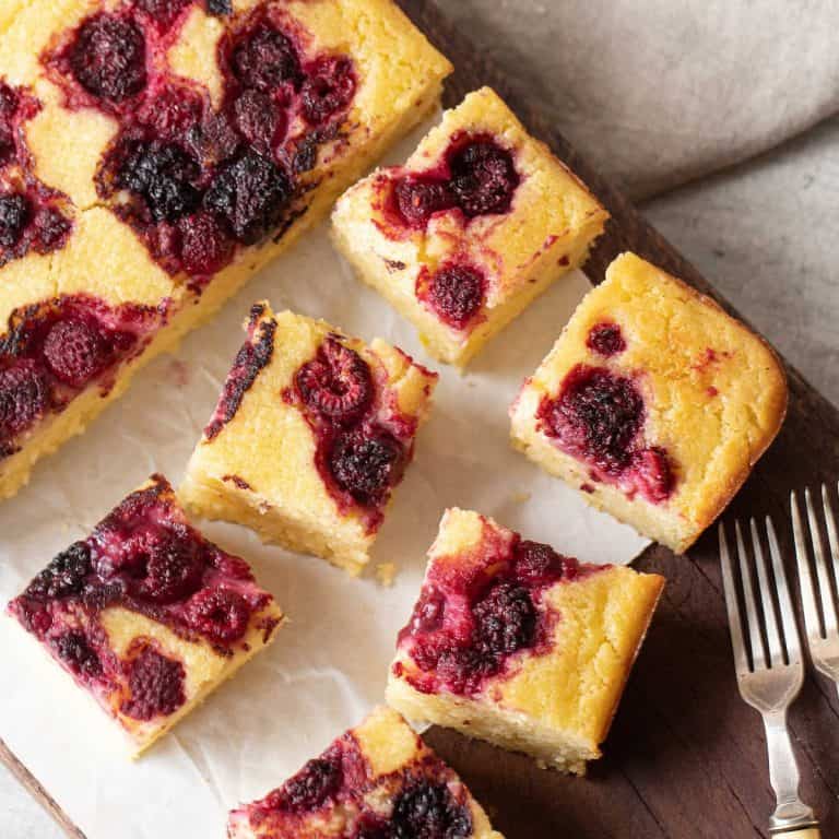 Close up overview of berry ricotta squares on white paper and a wooden board.