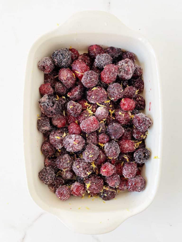 Cream-colored ceramic dish with frozen blackberries and lemon zest.