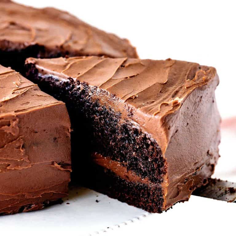 A piece of chocolate filled and frosted chocolate cake slice being removed from whole cake on a white cake stand. White background.