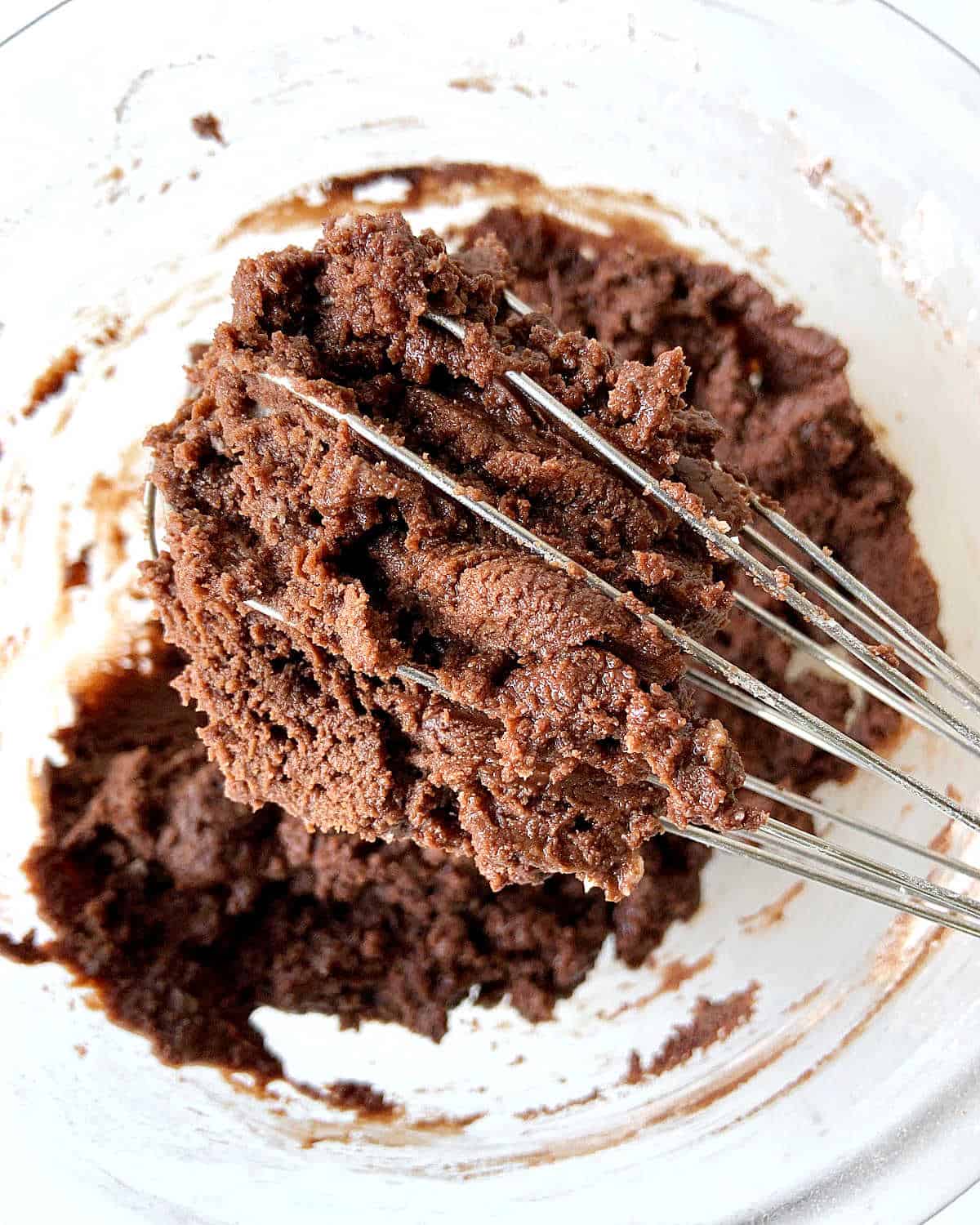 Grainy chocolate mixture lifted with a wire whisk from a glass bowl.