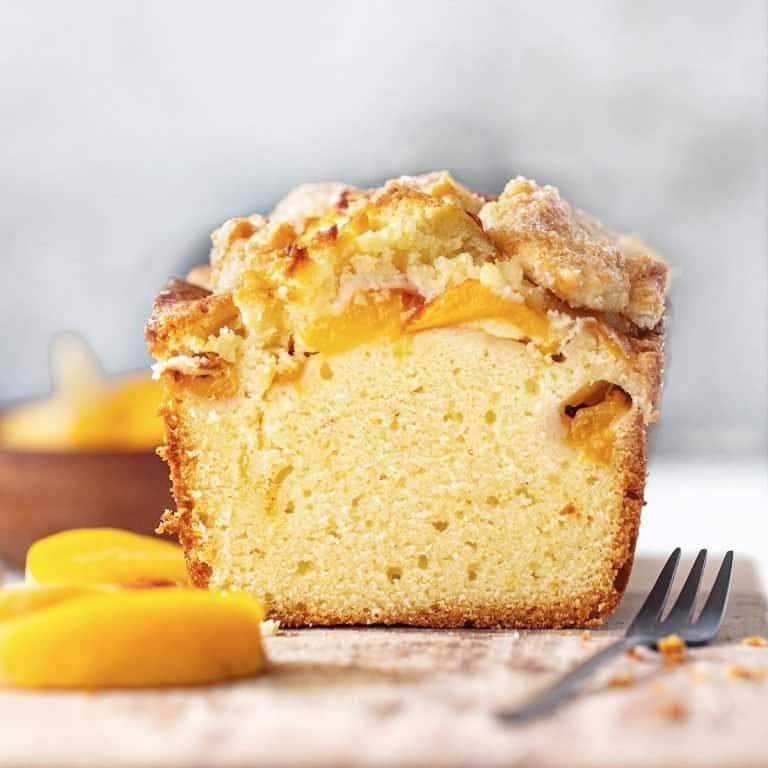 Front view of cut peach pound cake on wooden board. Grey background, peach slices, dark fork around.