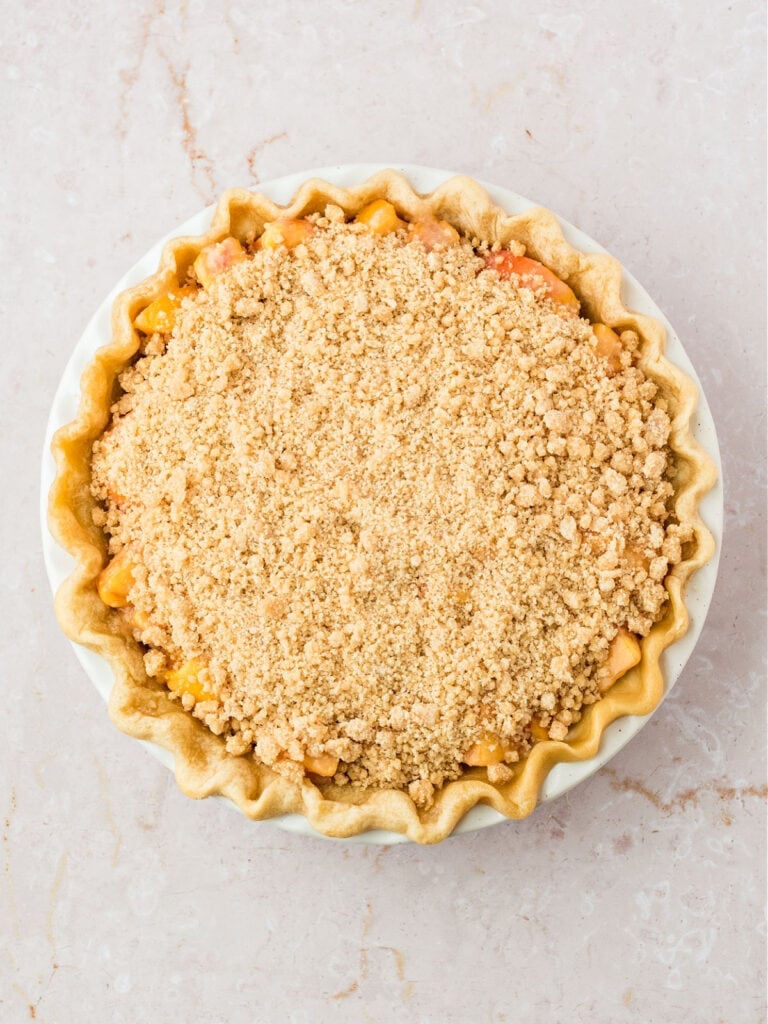Crumble-topped peach pie before baking. White pink background.