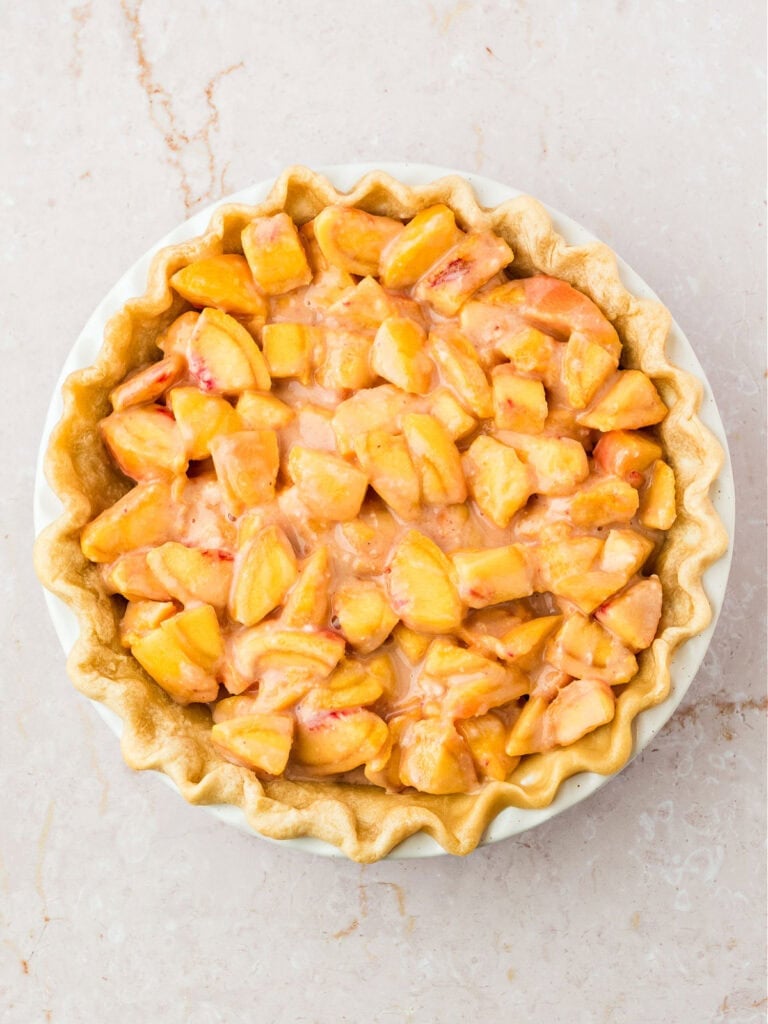 Filling for peach pie with crust in a pie plate. White pink surface.