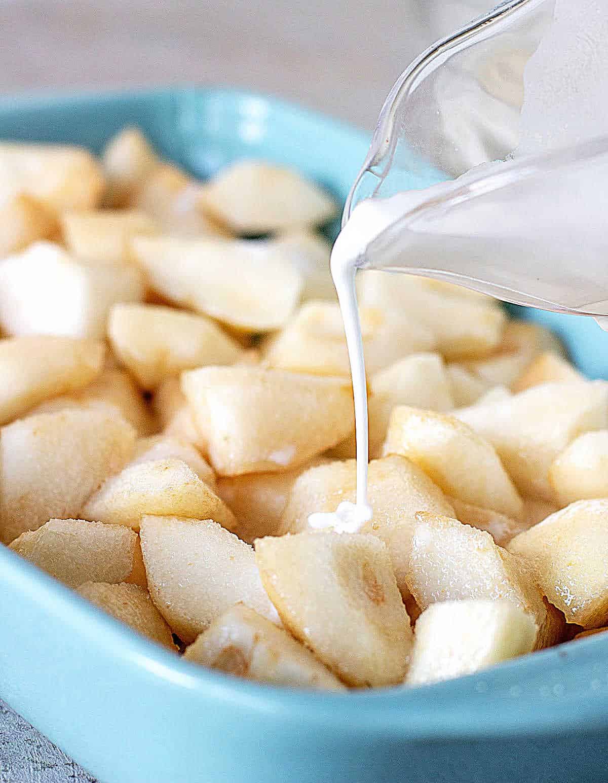 Pouring cornstarch slurry over pears chunks on blue ceramic pan