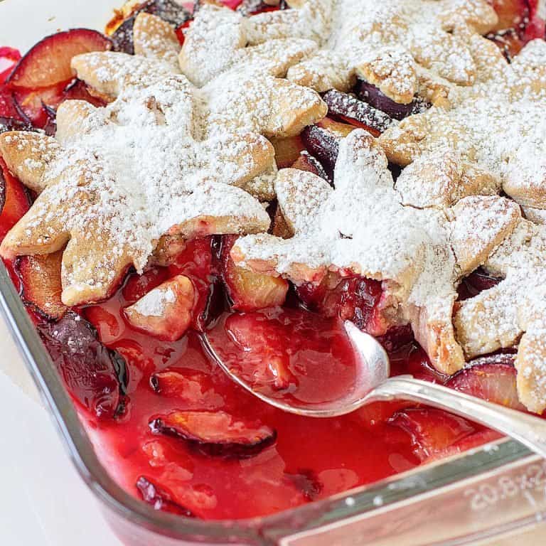 Silver spoon inside glass dish with plum cobbler.