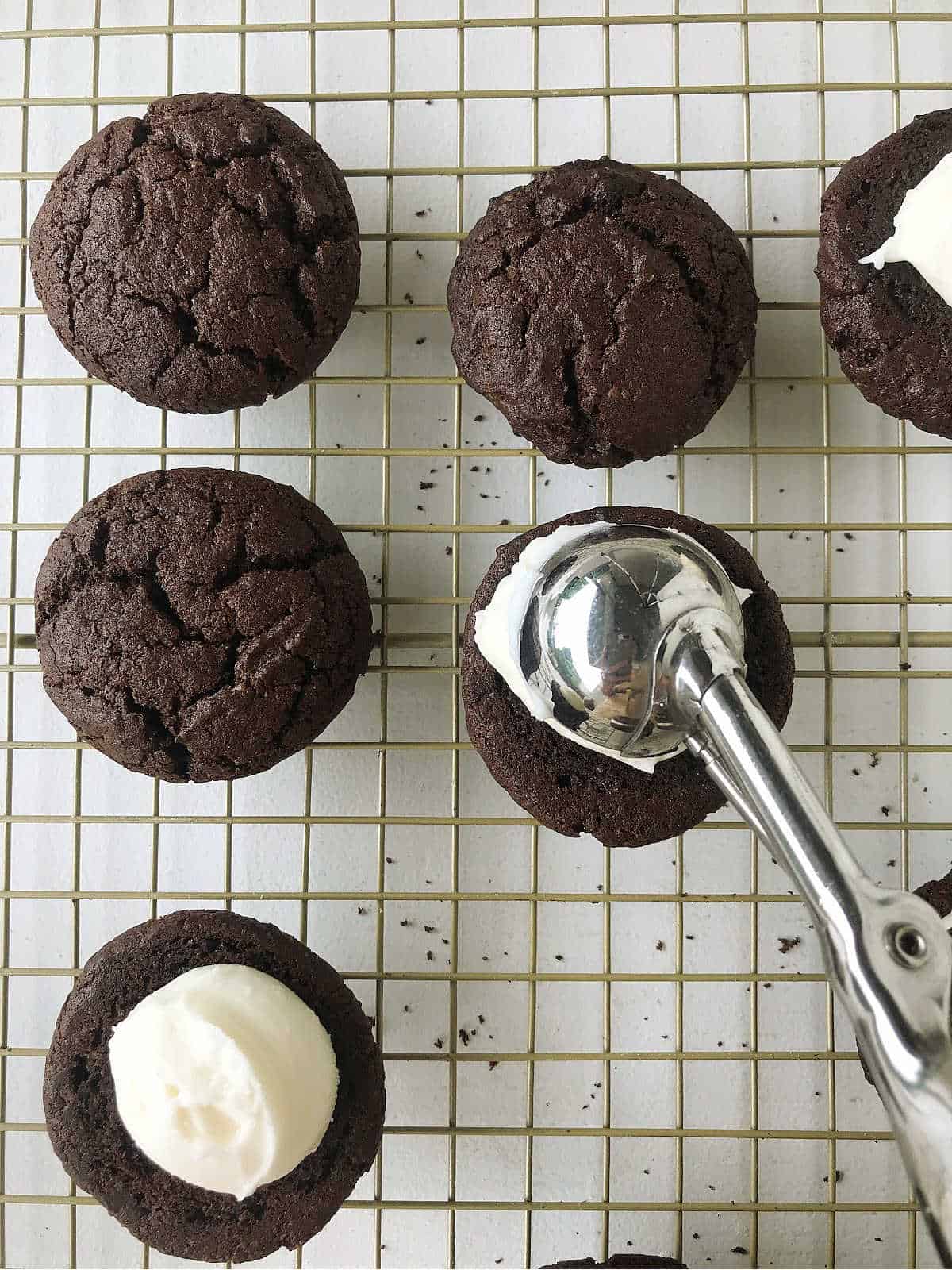 Scooping cream cheese filling on chocolate whoopie pie half on a wire rack.