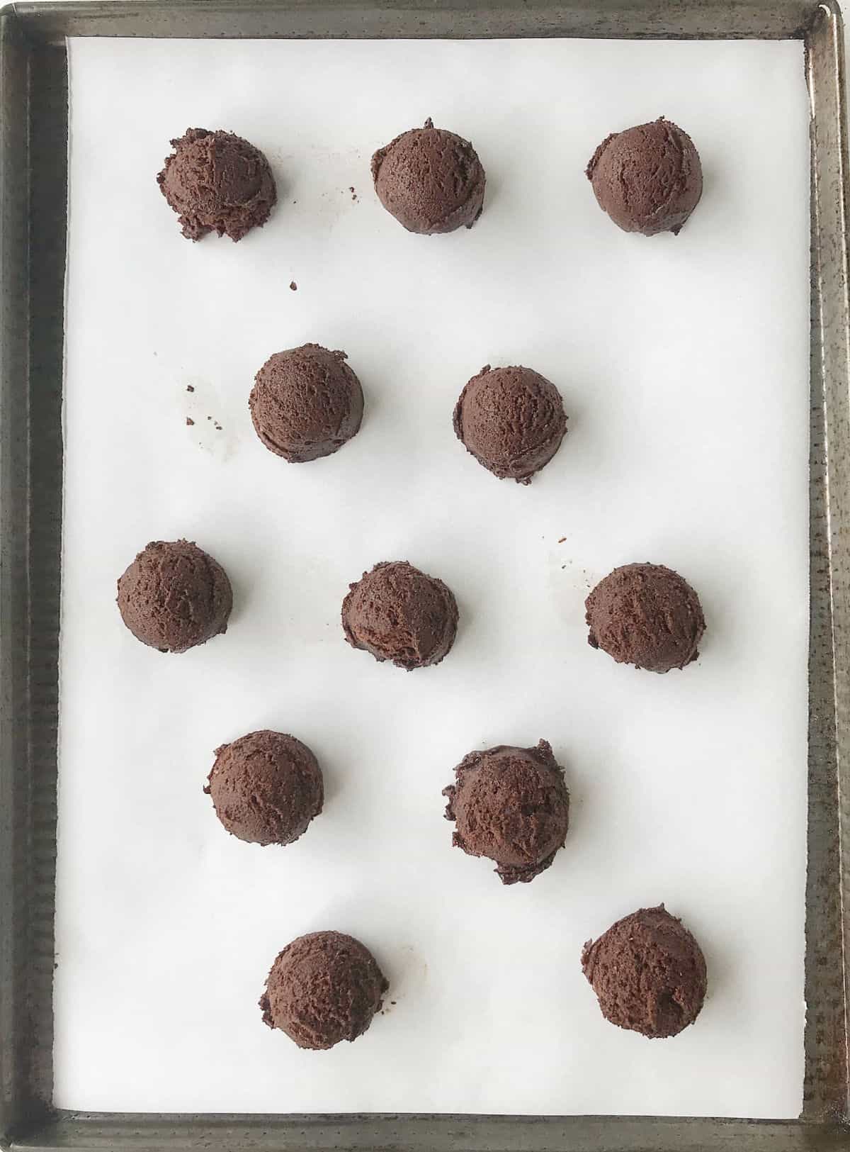 Top view of unbaked chocolate whoopie pie scoops on white paper on a cookie sheet.