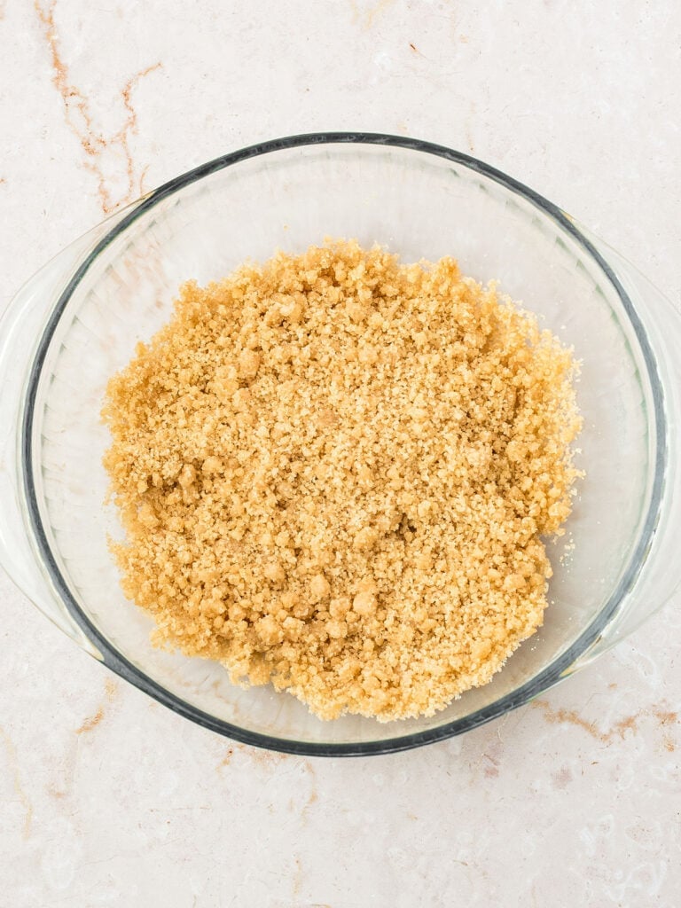 Glass bowl with crumble topping for pie. Whitish pink background.