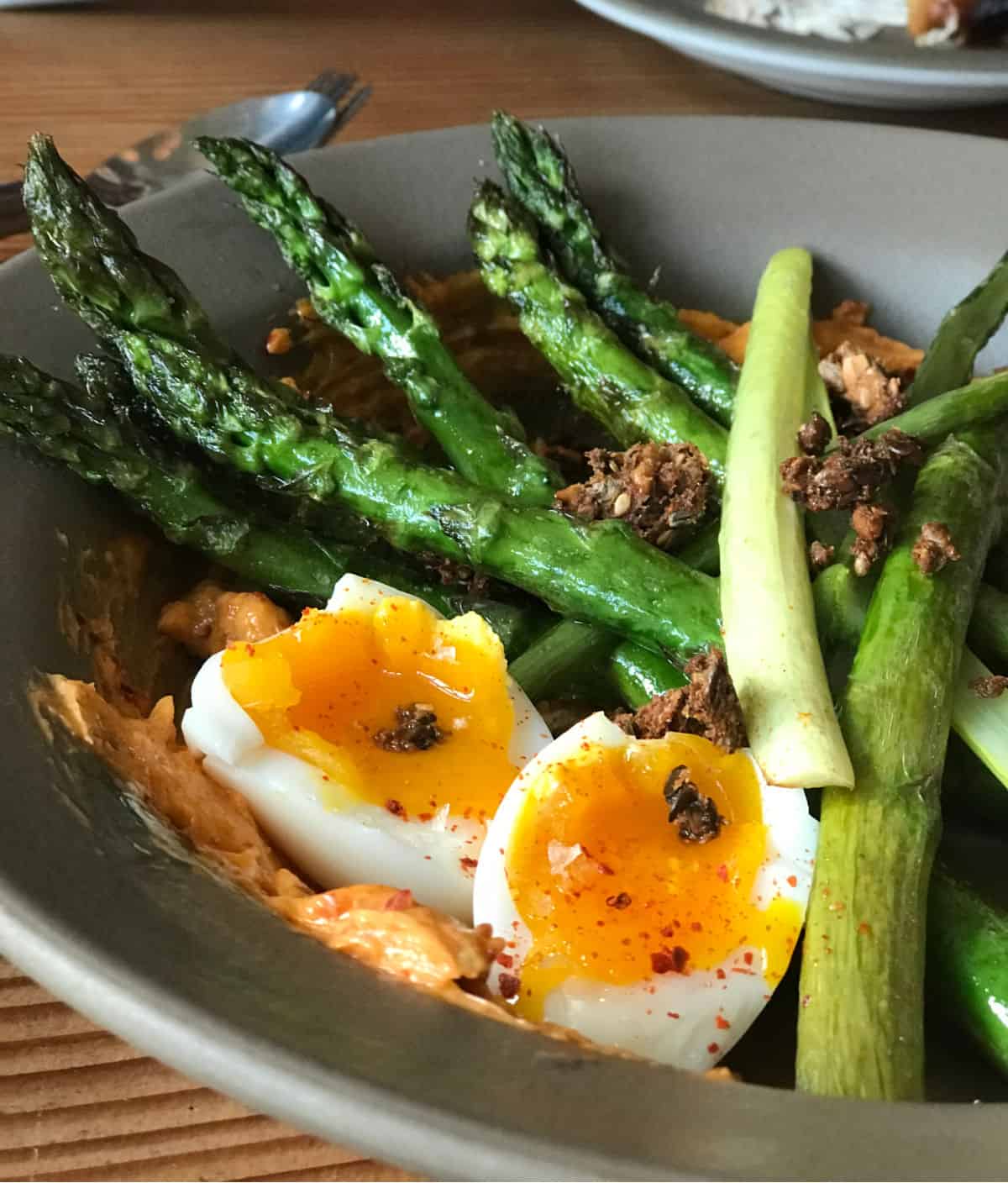 Grey bowl with halved egg, green asparagus, and green onion.