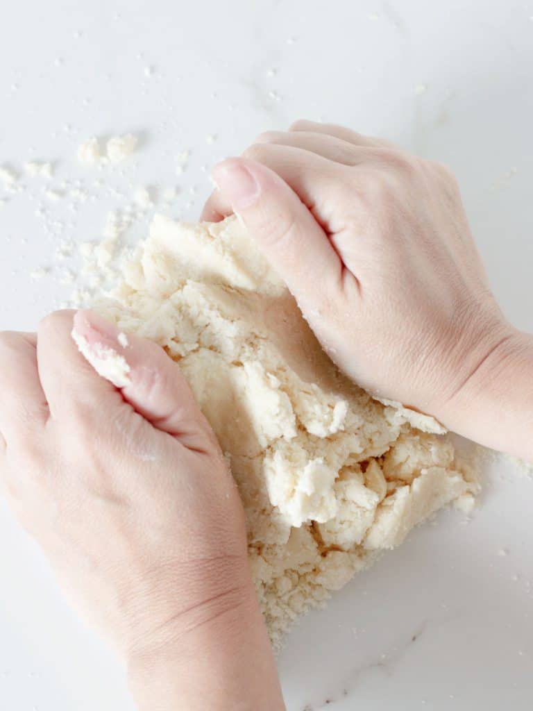 Pair of hands working a pie crust dough on a white marble surface.