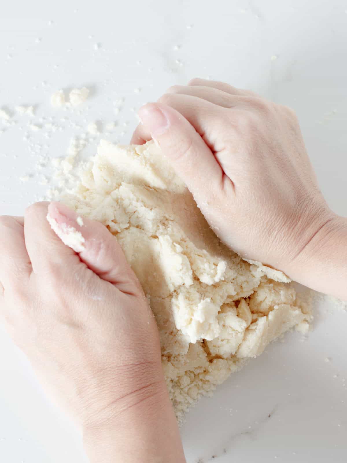 Pair of hands working a pie crust dough on a white marble surface.