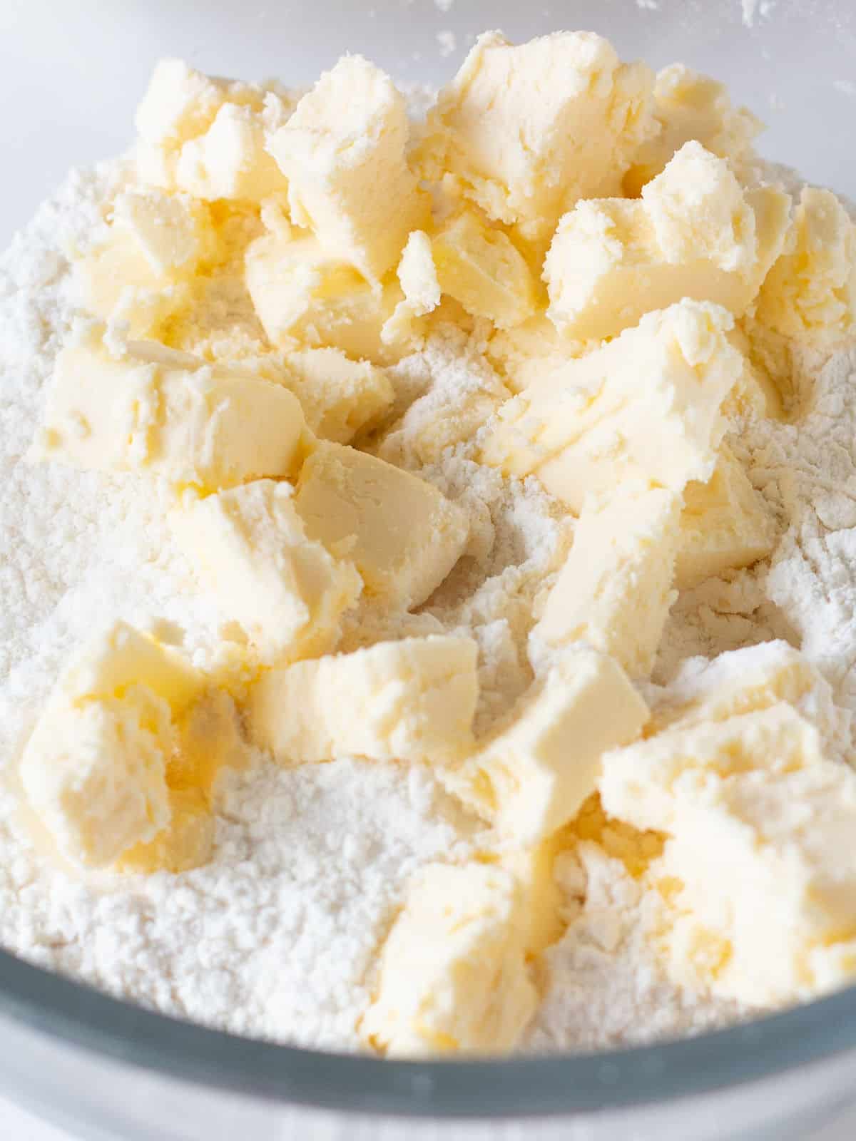 Close up of butter pieces with flour in a glass bowl.