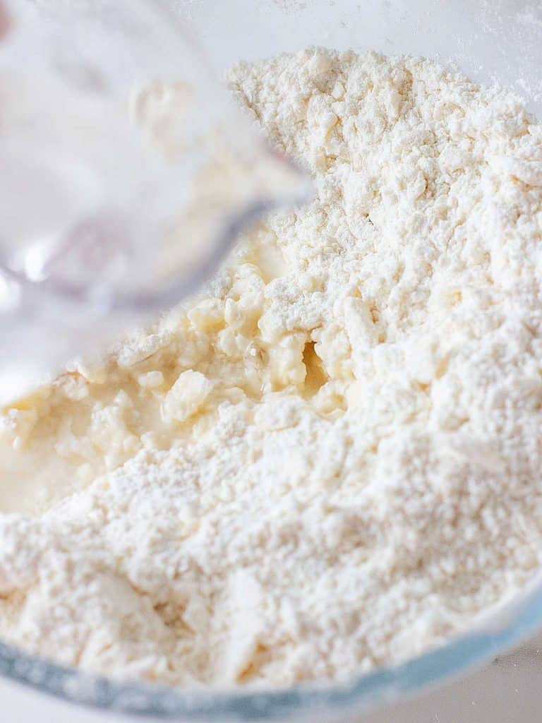Adding water to flour and butter crumble mixture in a glass bowl.