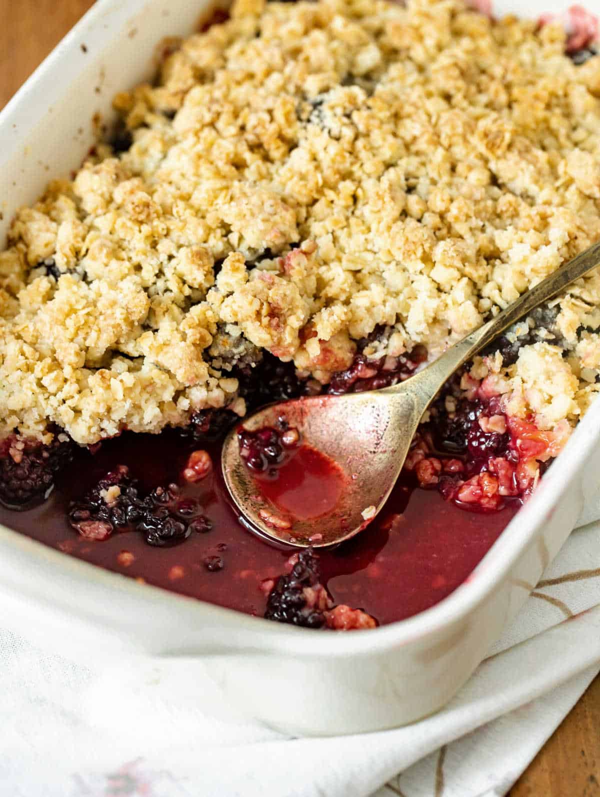 Eaten blackberry crisp on a whitish dish with a spoon inside.