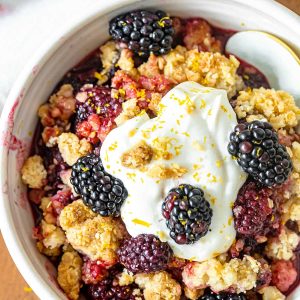 Very close up top view of blackberry crumble serving with whipped cream in a white bowl with a spoon.