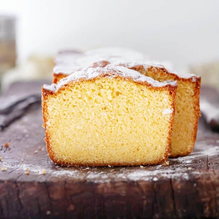Front view of sliced vanilla pound cake dusted with powdered sugar on a wooden board.