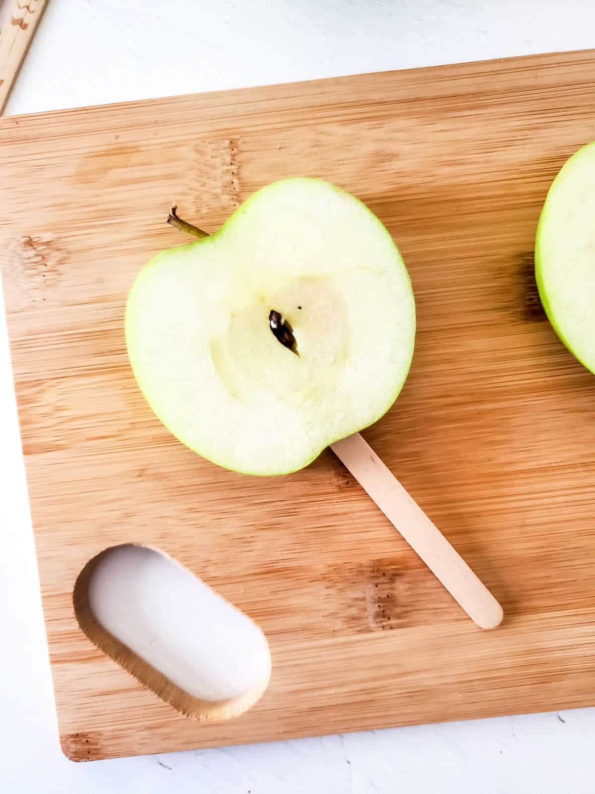 Single apple slice on a stick on a wooden board.