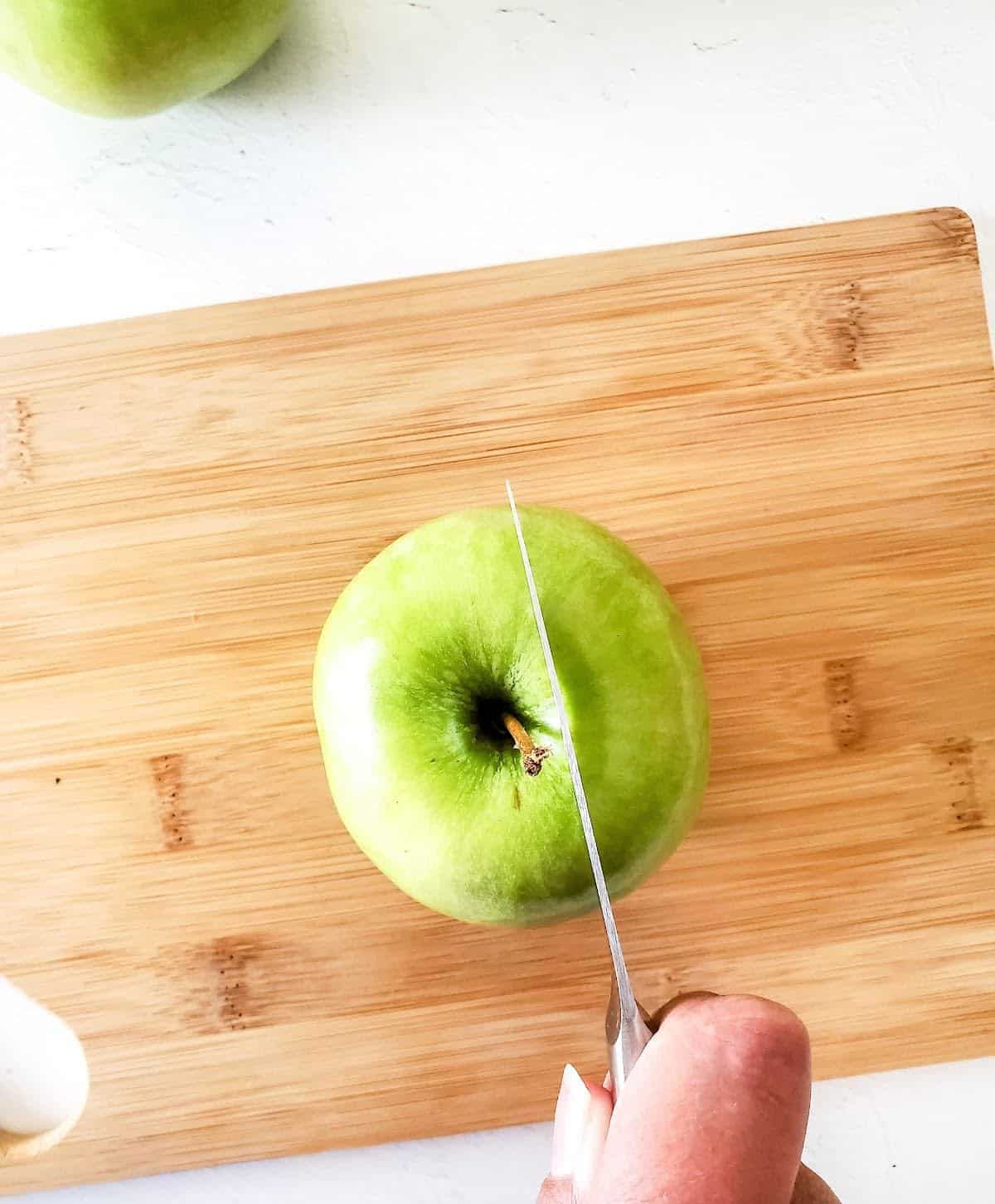 Cutting a green apple on a light wooden board with a kitchen knife.