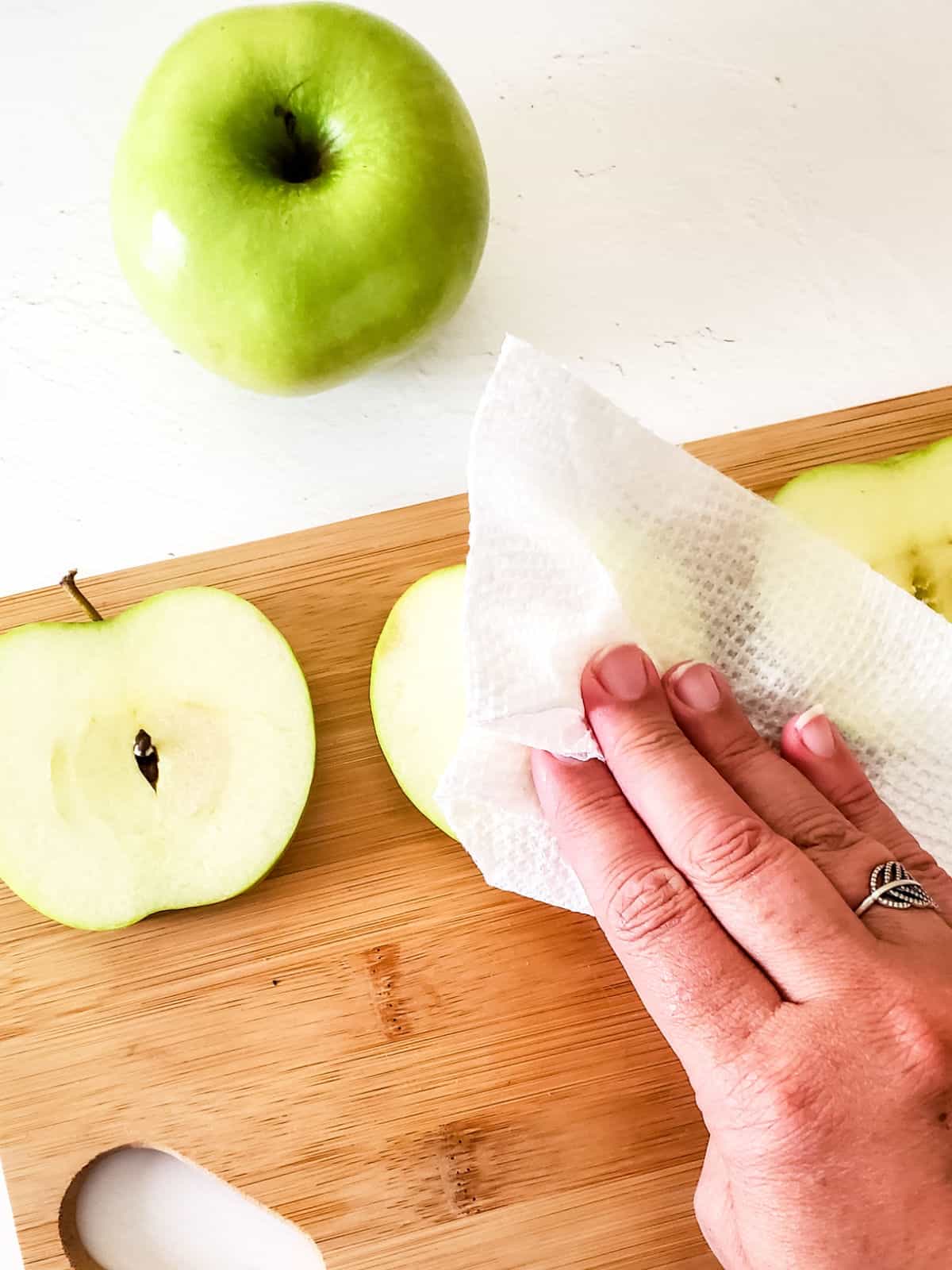 Hand blotting apple slices with paper on a wooden board. 
