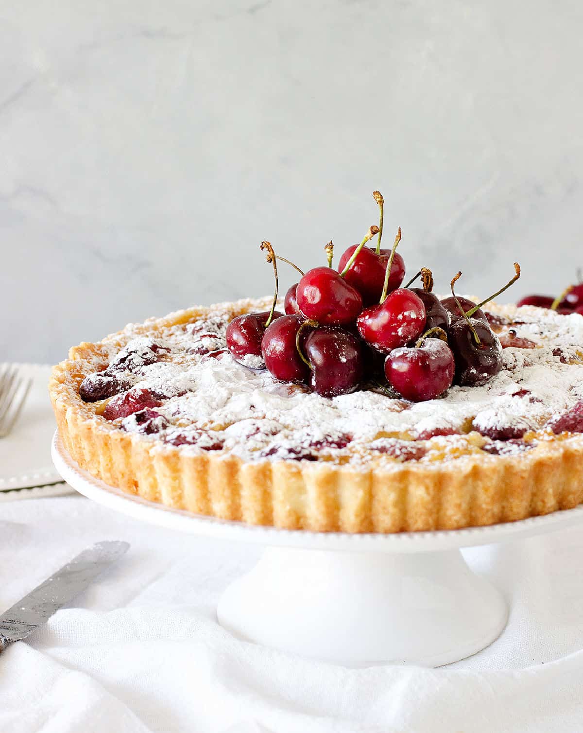 Whole cherry tart on a white pie plate. Fresh cherry topping. Grey background.